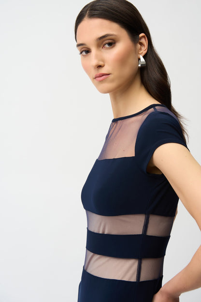 Woman wearing a navy blue dress with sheer panels on a white background